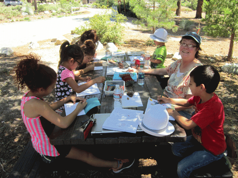 photo of instructor and children making art at picnic table